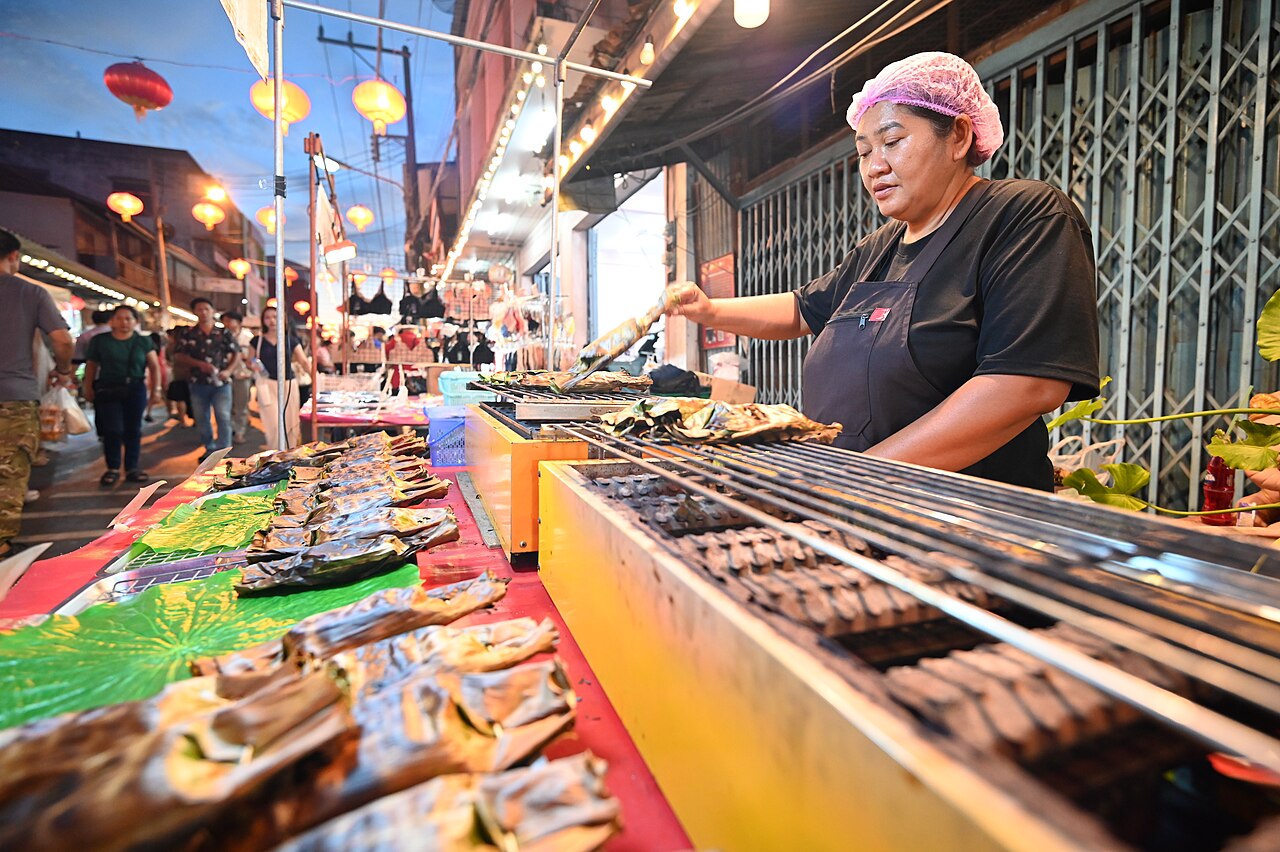 พ่อค้าย่างปลาเรียงแถวบนเตาถ่านที่ตลาดยามค่ำ แสงไฟและควันลอย — บรรยากาศปิ้งย่างซีฟู้ดริมหาดจอมเทียน พัทยา