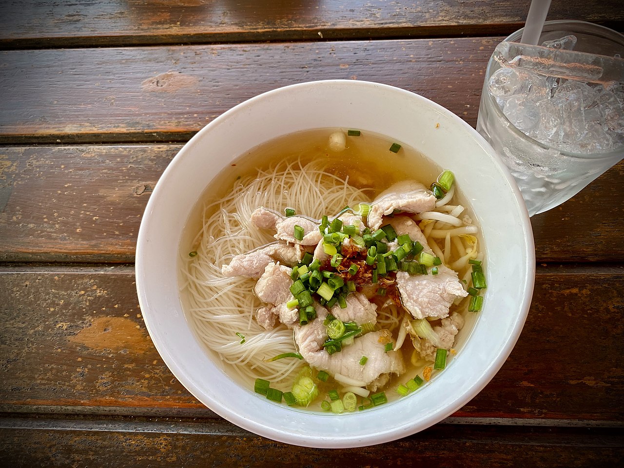 A bowl of clear Thai pork noodle soup in Phuket, topped with spring onion and fried garlic, an example of the everyday Thai food found across the island