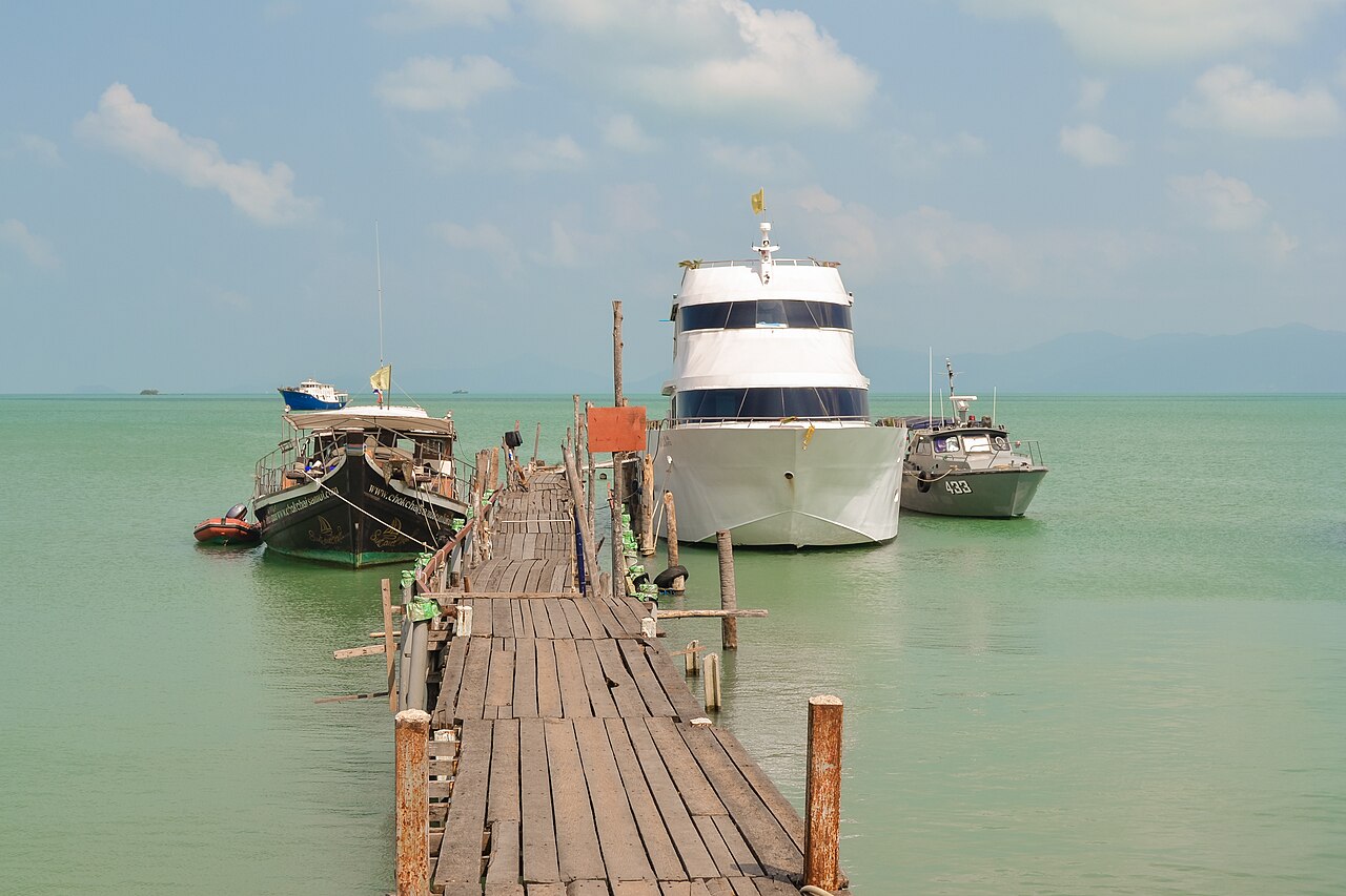 สะพานไม้ท่าเรือหมู่บ้านชาวประมงบ่อผุด เกาะสมุย ทอดยาวลงทะเลอ่าวไทย มีเรือจอดเทียบท่า