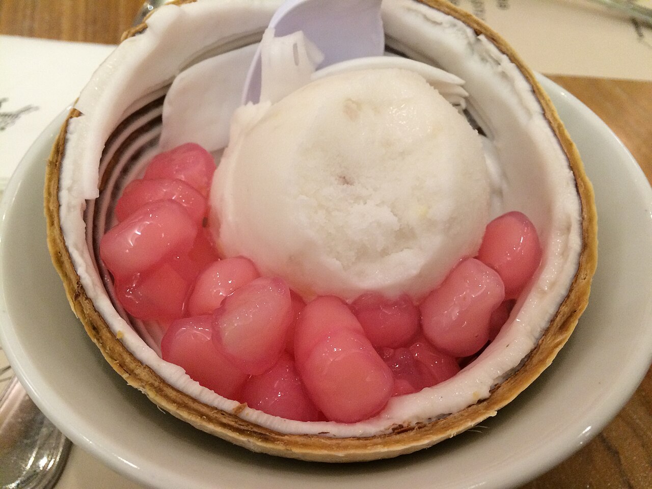 Coconut ice cream served inside a halved young coconut, topped with pink water-chestnut rubies