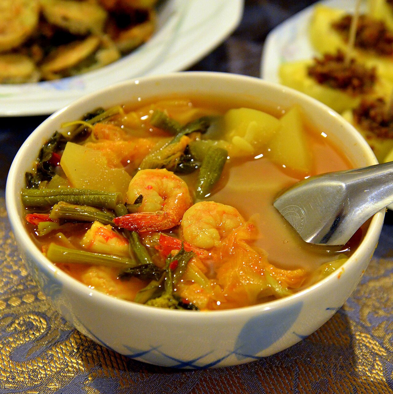 A bowl of southern Thai sour curry with prawns and vegetables in a deep orange turmeric broth