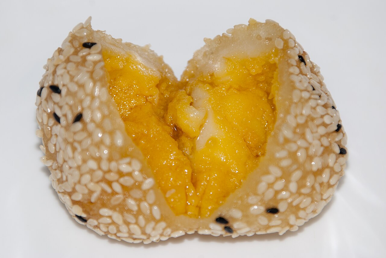 A jian dui, a sesame-coated fried glutinous ball split open to show its golden sweet filling, crisp outside and chewy inside