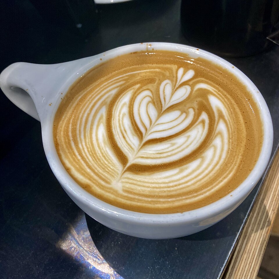 A latte with leaf art on the surface in a ceramic cup