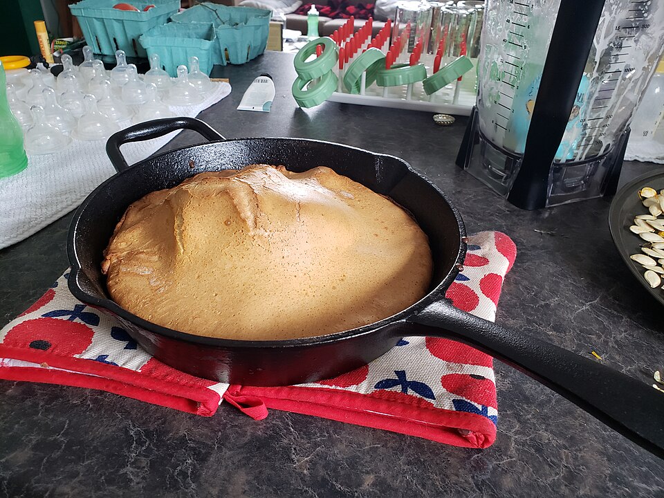A puffy Dutch baby pancake baked in a cast-iron pan dusted with sugar and lemon