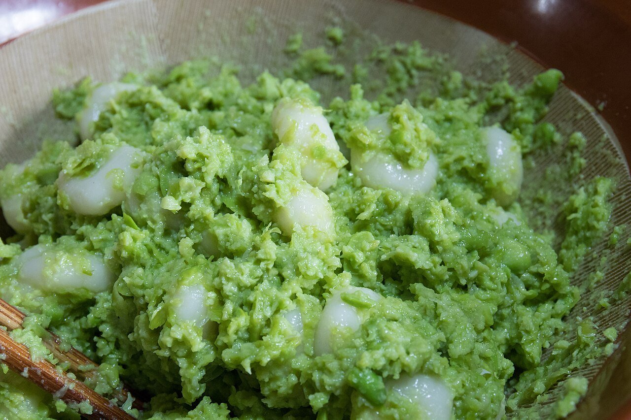 Zunda mochi: five soft white rice cakes arranged in a bamboo tray, coated generously in a vivid green edamame paste with a slightly textured, creamy consistency
