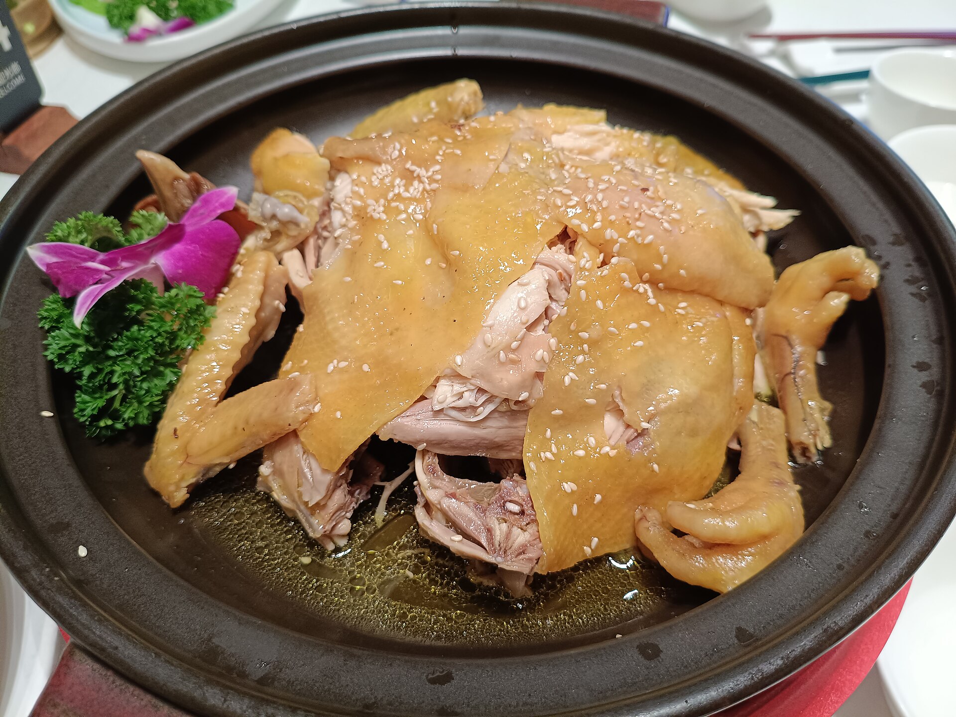 Hakka salt-baked chicken, a whole chopped bird in a clay dish with glossy golden skin sprinkled with sesame
