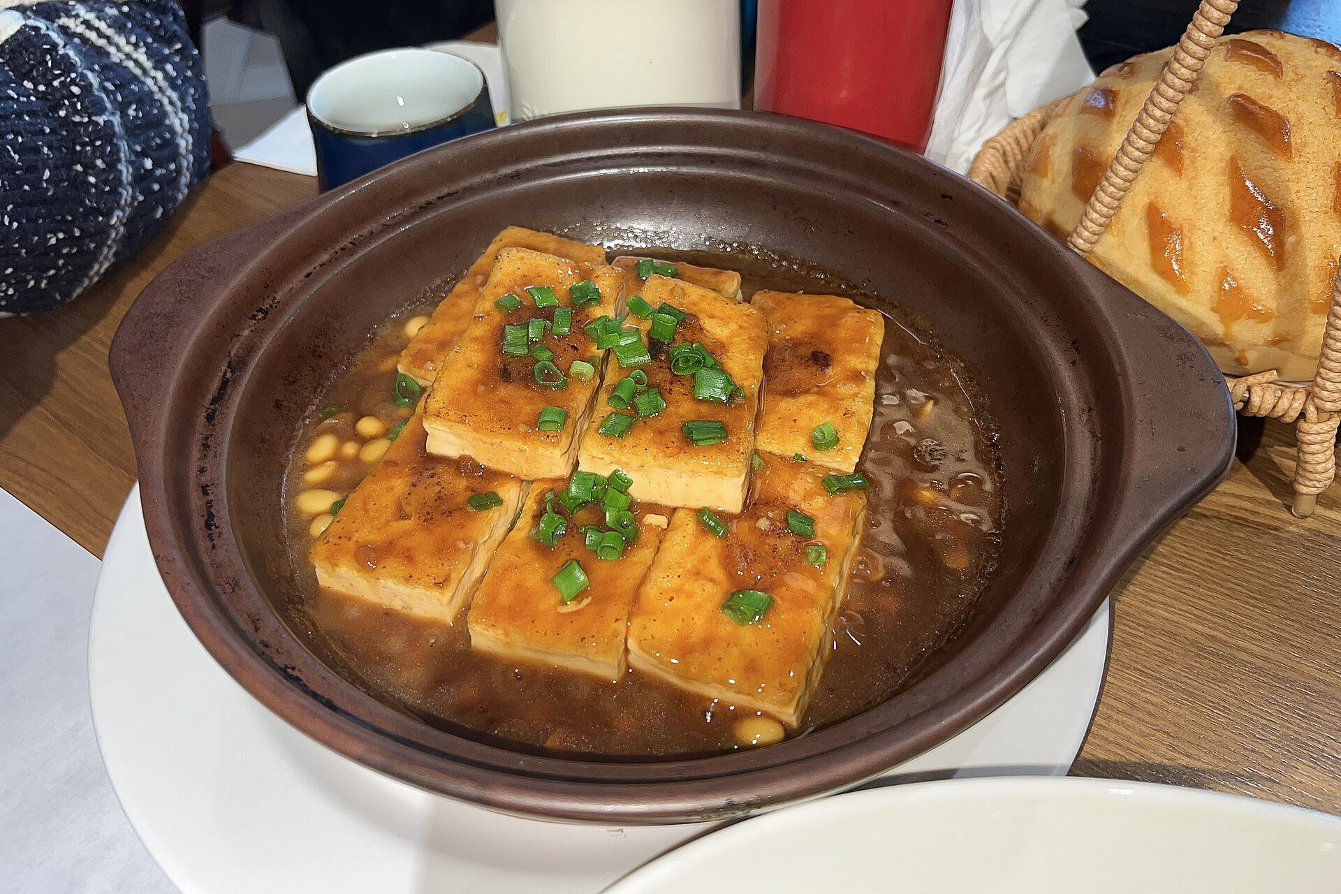 Hakka stuffed tofu, golden tofu blocks arranged in a clay pot with a savoury sauce and chopped spring onion