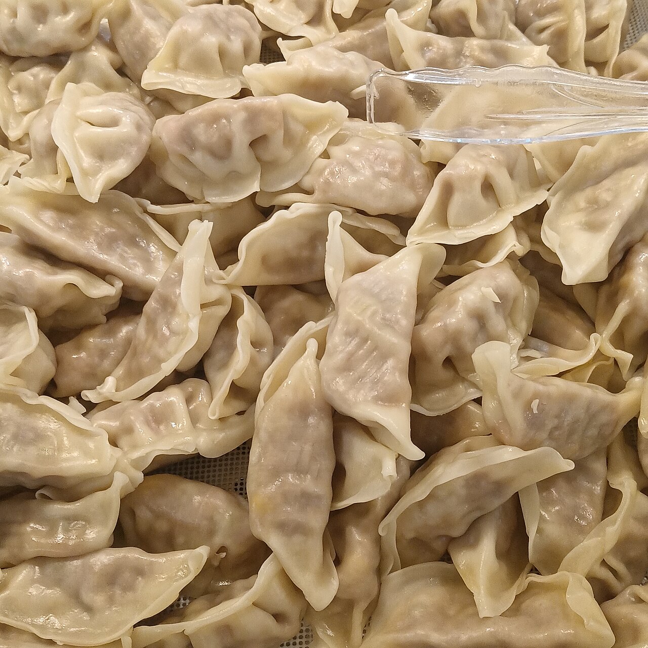 A large heap of boiled Xi'an jiaozi with thick, soft pale wrappers, the meat filling faintly visible through the dough