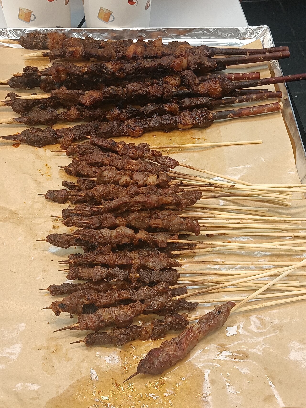 เสียบไม้เนื้อแกะย่างถ่านโรยยี่หร่าและพริกป่นจำนวนมากวางเรียงบนถาด