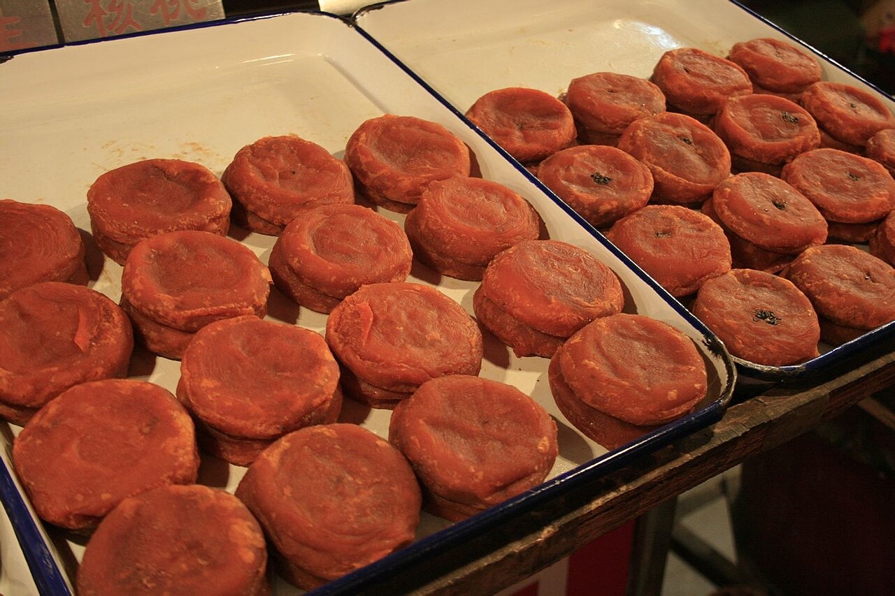 Golden-orange fried persimmon cakes (huanggui shizibing) laid out in white enamel trays at a stall in Xi'an's Muslim Quarter