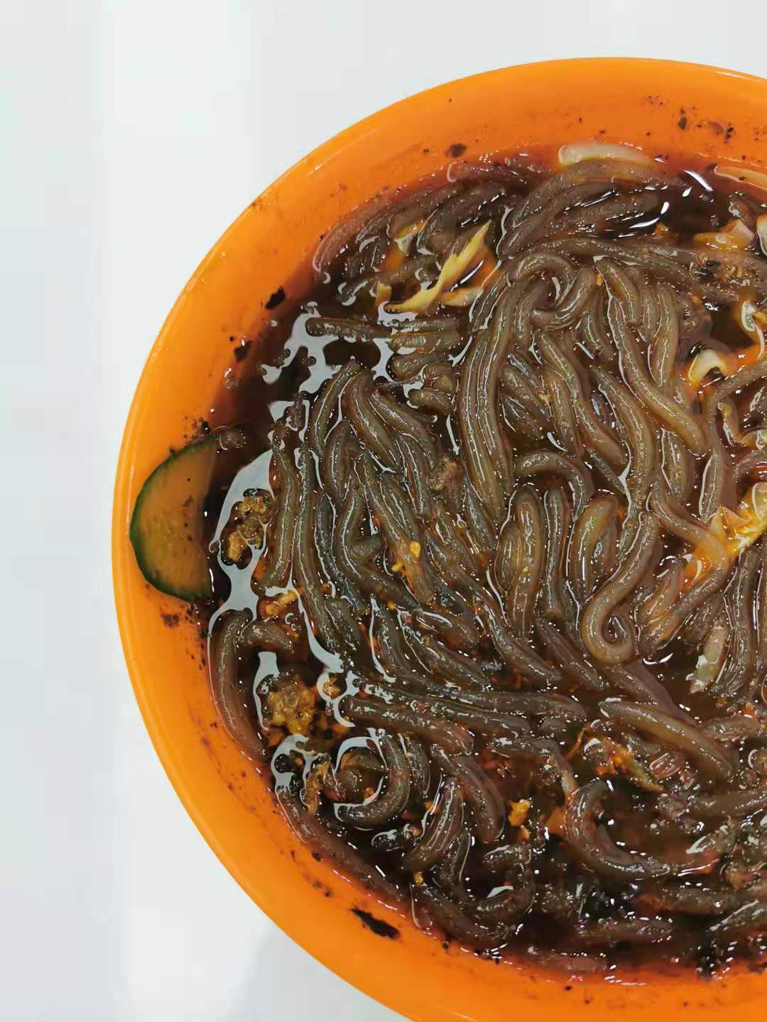 Suan la fen — translucent sweet-potato glass noodles in a dark hot-and-sour chilli-oil broth with cucumber, in an orange bowl