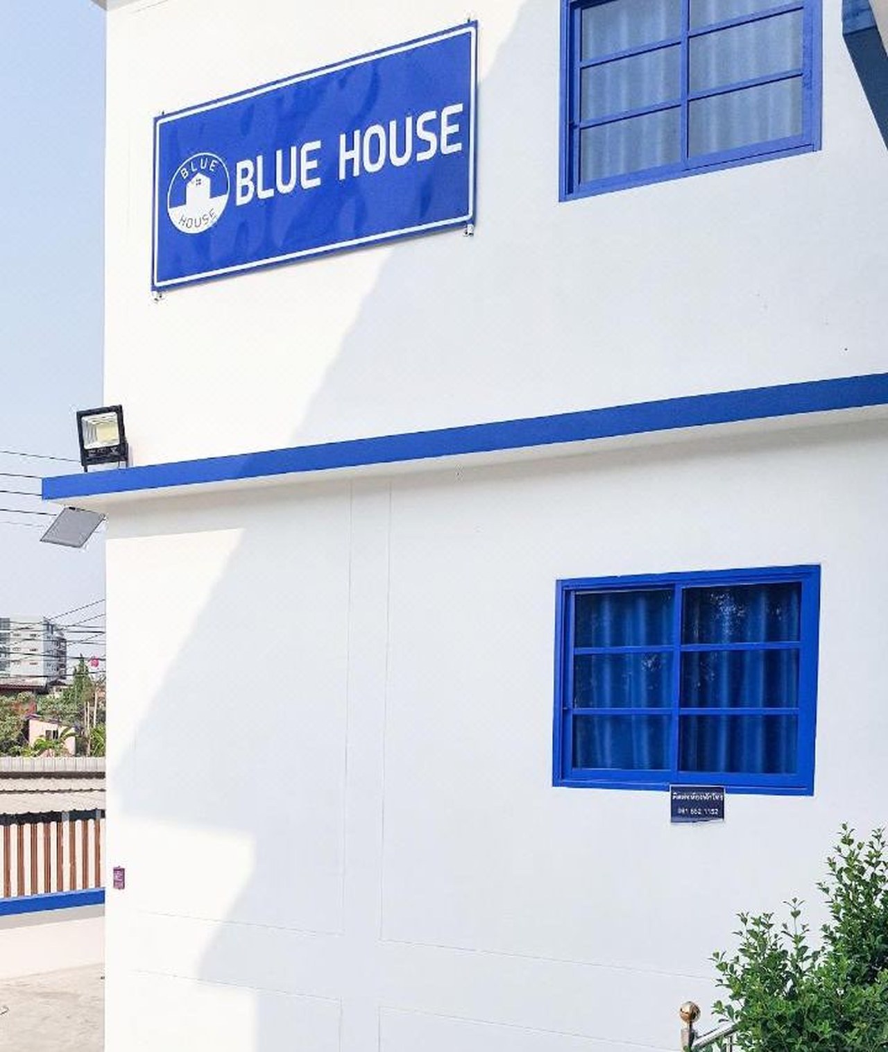 ป้าย Blue House สีน้ำเงินบนผนังตึกสีขาวของที่พักในเมืองอ่างทอง