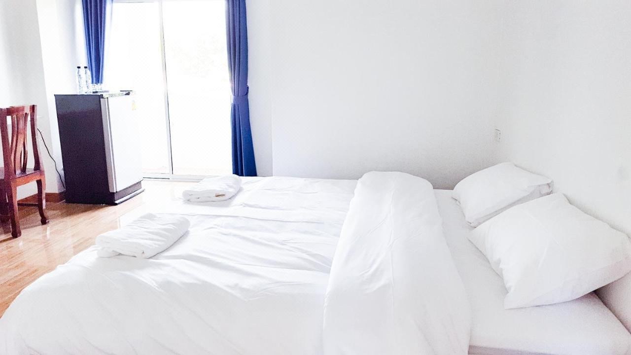 ห้องพัก Deluxe เตียงใหญ่ ผ้าปูขาว ผ้าม่านสีน้ำเงิน และประตูระเบียง