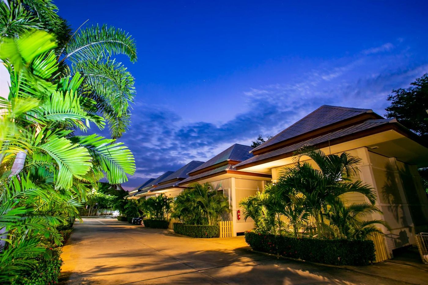 แถวบ้านเดี่ยวชั้นเดียวของ Bualuang Boutique Resort ยามค่ำ มีไฟอุ่นและต้นปาล์ม