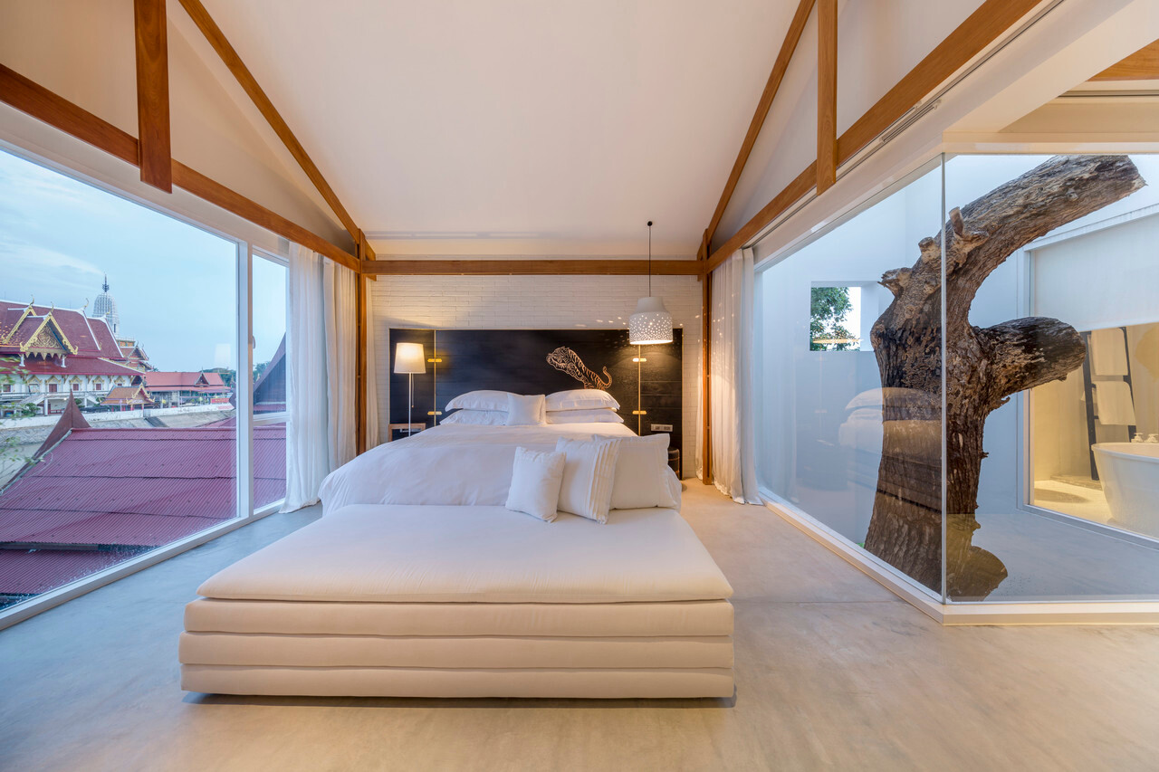 White-on-white room with dark timber beams and full-height glass looking out to the temple roof across the river