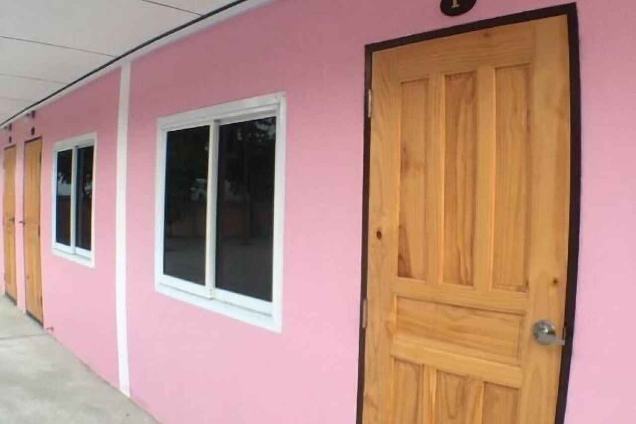Single-storey pink room block at Smile Resort Ang Thong with wooden doors and parking outside each room