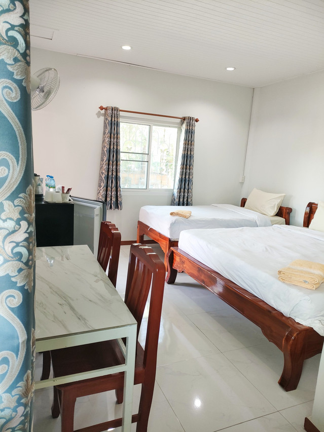 Twin-bed guest room interior with a window, fridge, marble-top table and fan
