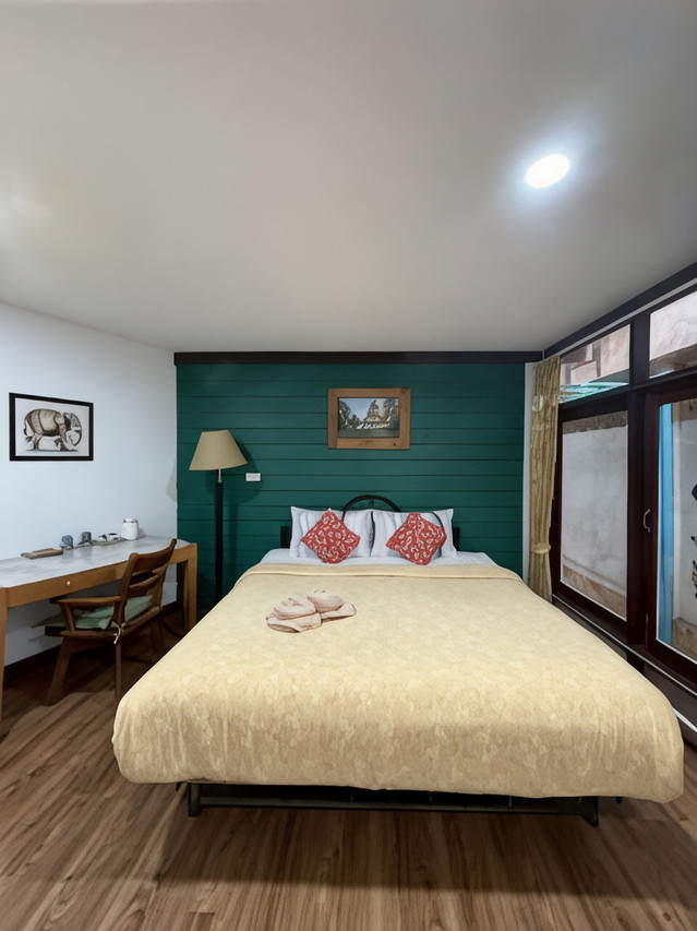 Guest room with green-painted timber wall, silk-draped bed and wooden desk at Tamarind Guesthouse