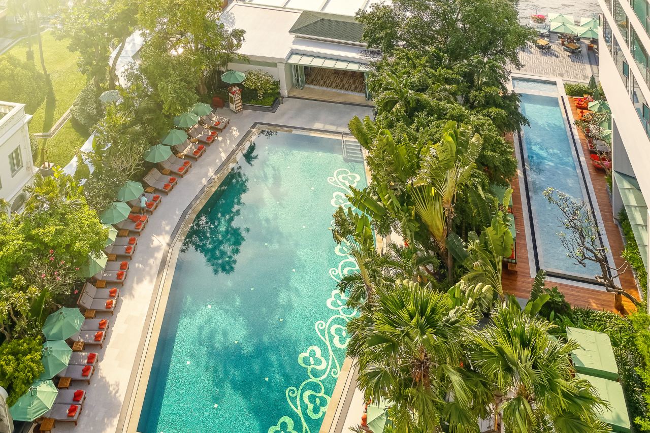 Riverside swimming pool surrounded by palm gardens and green-and-orange umbrellas