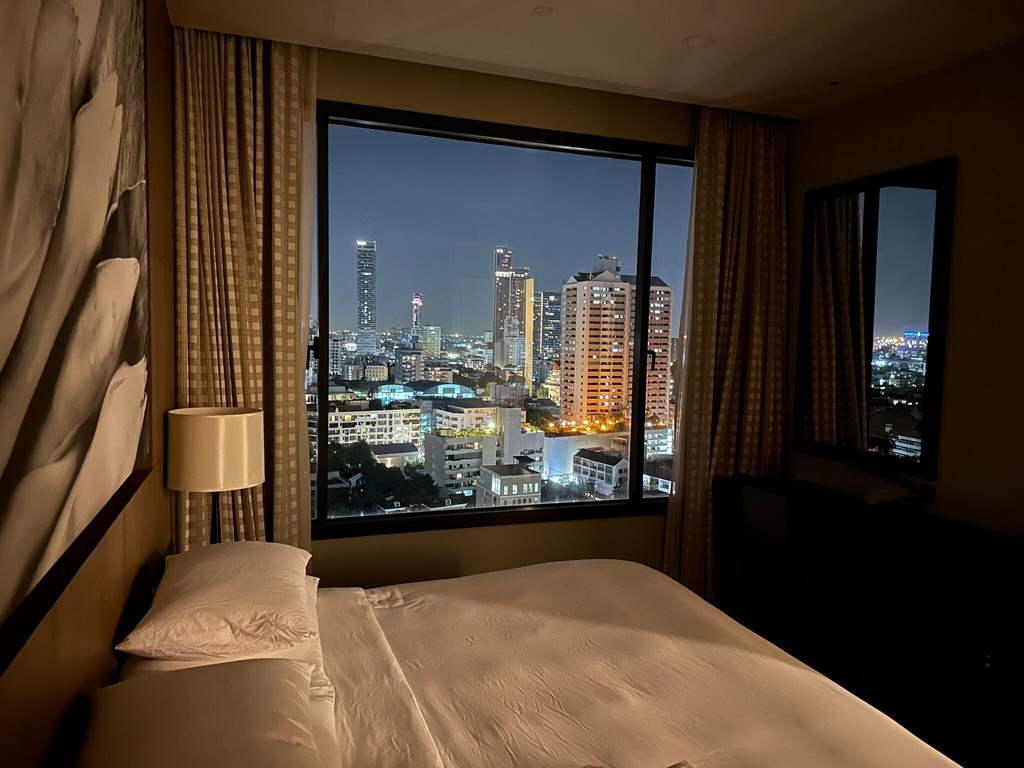 Suite bedroom at night with a full-window view of the Bangkok city lights