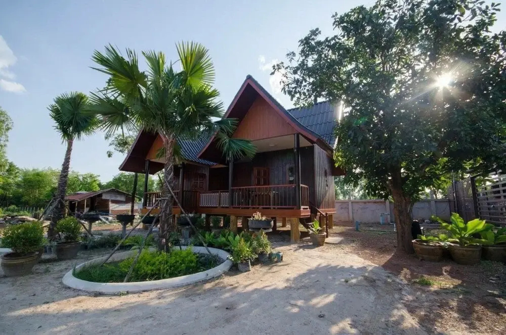 บังกะโลไม้สักยกพื้นทรงจั่วของ The Little Garden Resort ท่ามกลางต้นปาล์มในสวน