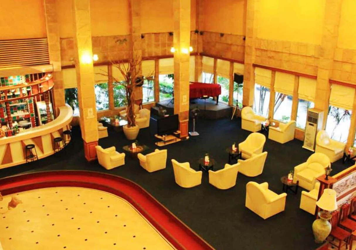 Tall stone-pillar lobby lounge with cream armchairs and a grand piano at Thepnakorn Hotel