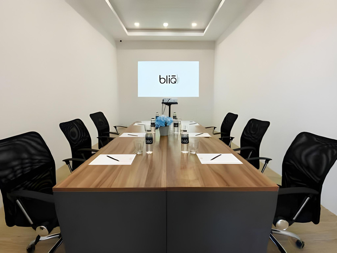 Meeting room with long wood table, office chairs and a projected bliQ logo