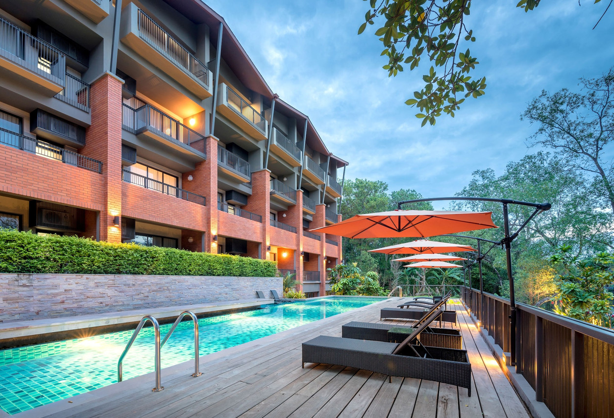Outdoor pool beside the brick building with sun loungers and orange umbrellas at D Varee Diva Rimnaam