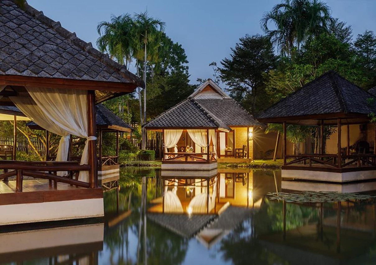 Wooden Lanna salas reflected in a lily pond at dusk at Phowadol Resort Chiang Rai