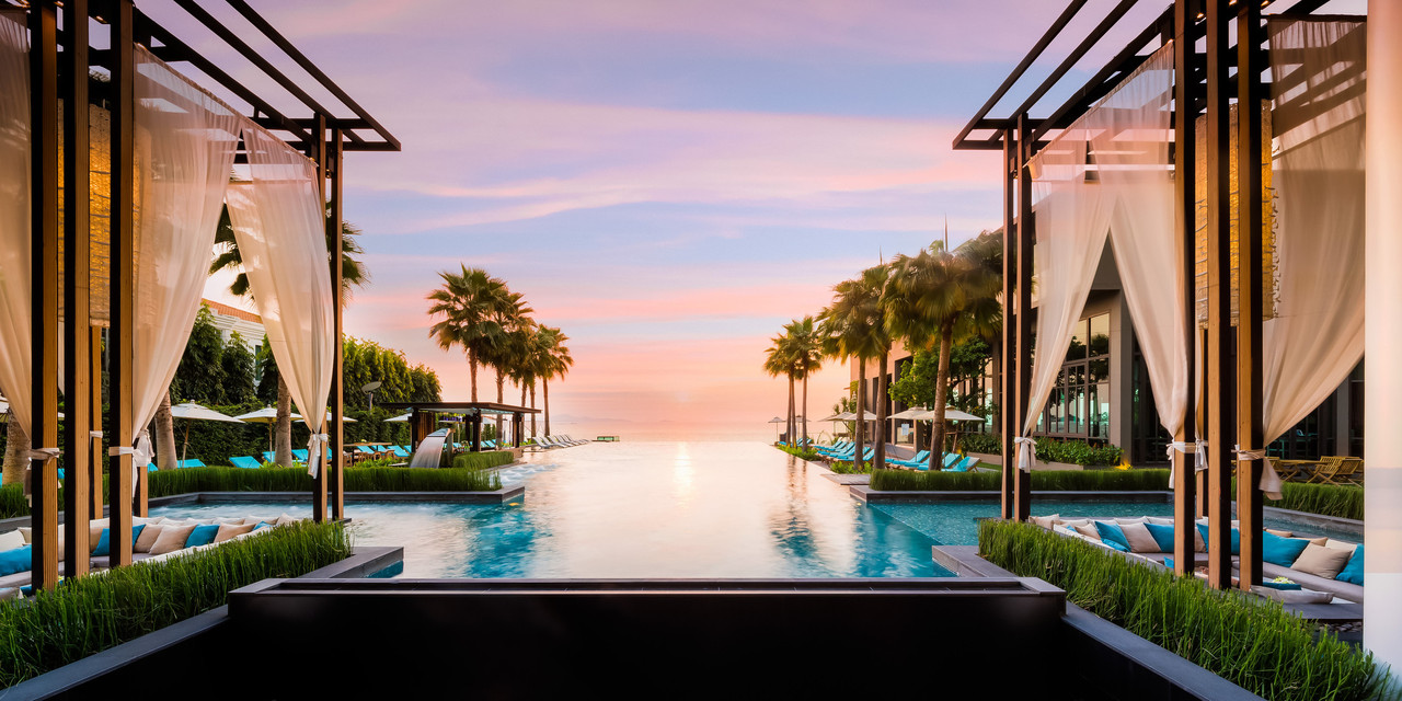 Sea-facing infinity pool with white-curtained cabanas at sunset, Pattaya Bay view, Chonburi