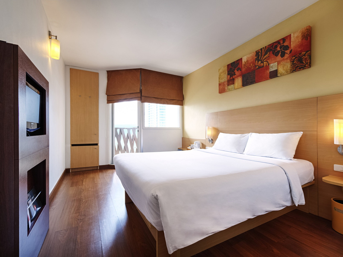 Standard Double room at ibis Pattaya with white bedding, wood floor and a small balcony