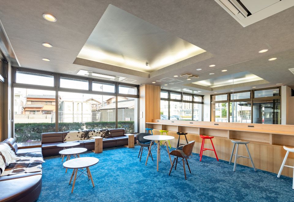 Bright shared lounge with blue carpet and colorful chairs at EN HOTEL Ise renovated 2023