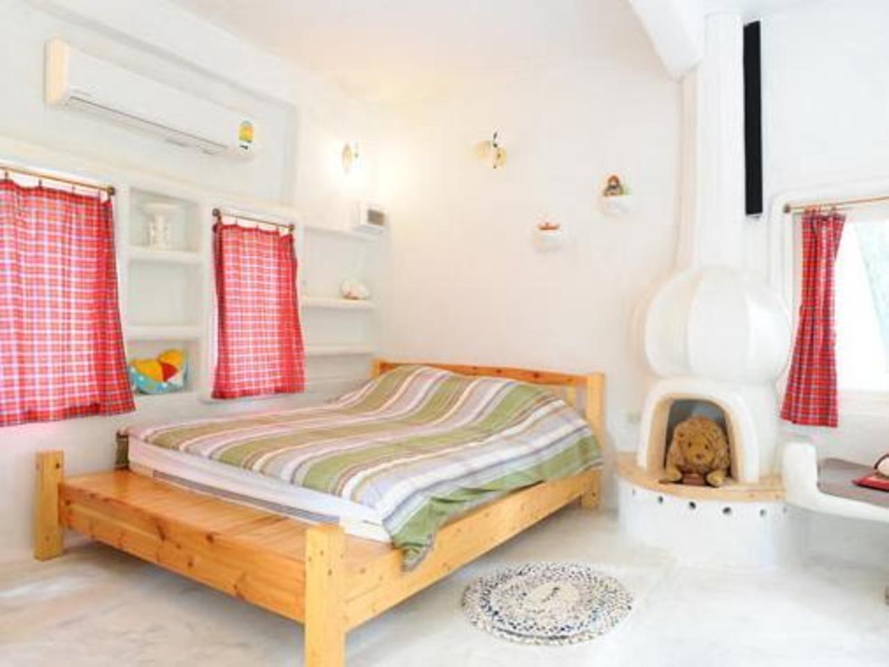ห้องพักผนังปูนปั้นสีขาว เตียงไม้บนแท่น เตาผิงปูนปั้น ผ้าม่านลายสก็อต Scenic Riverside Resort