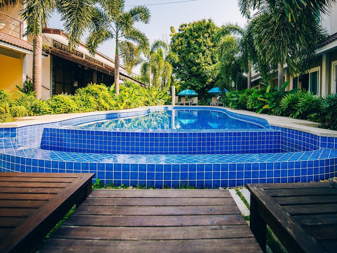สระว่ายน้ำกลางแจ้งกระเบื้องสีฟ้าและสวนปาล์มที่ Good Times Resort กาญจนบุรี