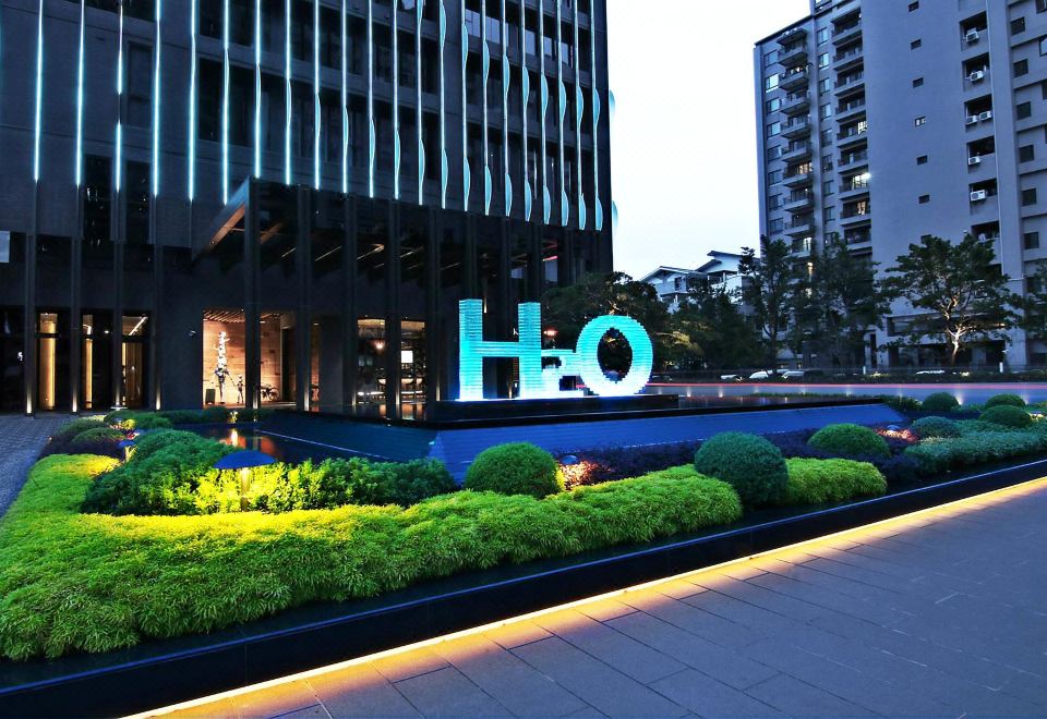 H2O Hotel Kaohsiung entrance at dusk with illuminated H2O sculpture in landscaped forecourt