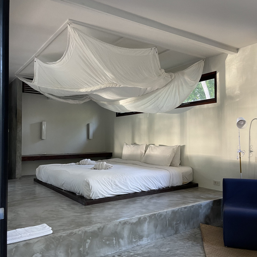 Interior of a polished-concrete cabana with a raised platform bed and draped mosquito net
