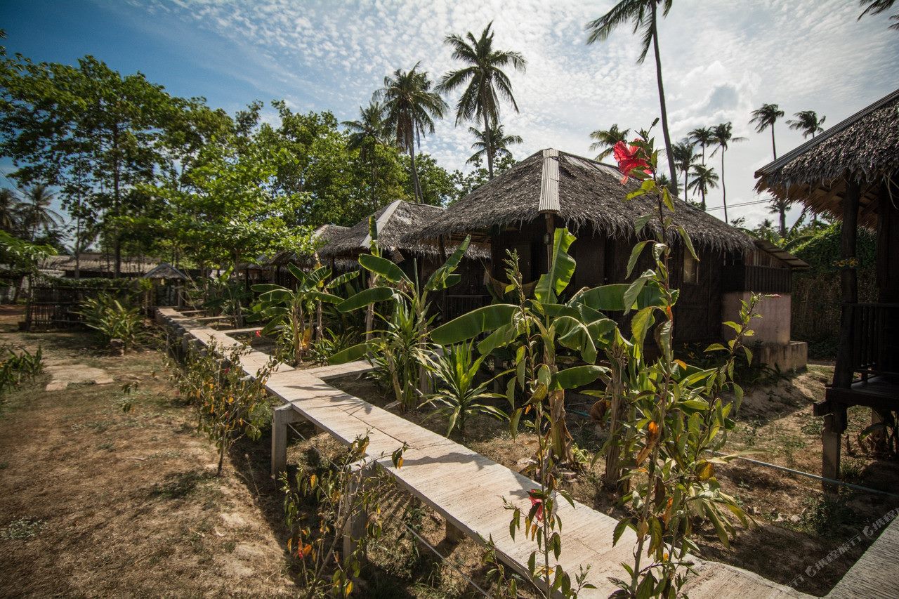 ทางเดินไม้ยกพื้นทอดผ่านบังกะโลหลังคาจากของ Mook Lanta Eco Resort