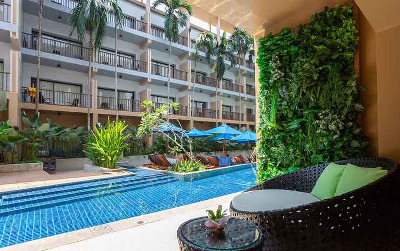 สระลากูนพร้อมเก้าอี้ริมสระและผนังต้นไม้เขียวที่ Deevana Plaza Krabi