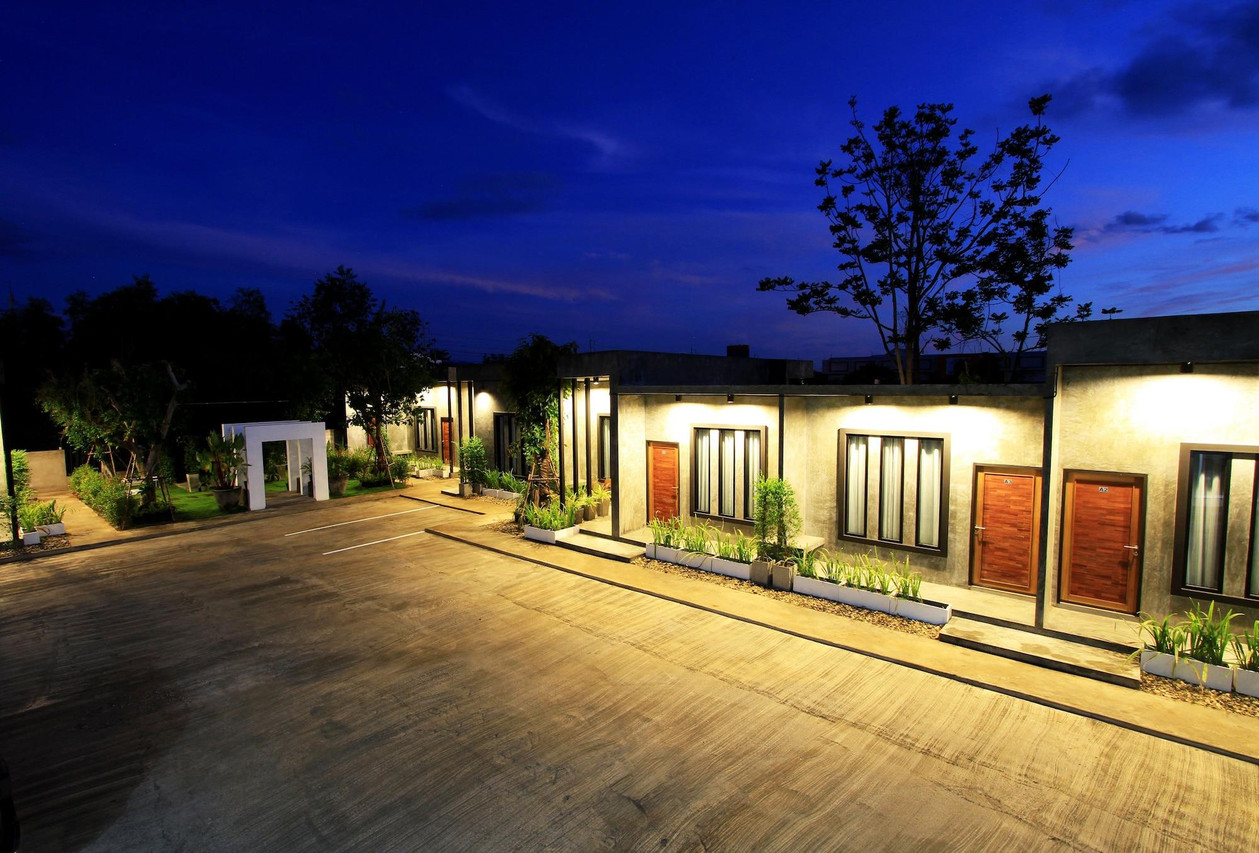 บรรยากาศกลางคืน แถวห้องชั้นเดียวเรียงรอบลานจอดรถ ไฟส่องอบอุ่น
