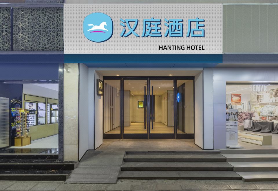 The Hanting Hotel Lijiang Ancient Town (汉庭酒店丽江古城大水车店) building at dusk, lit by the brand's signature blue 汉庭酒店 HANTING HOTEL sign