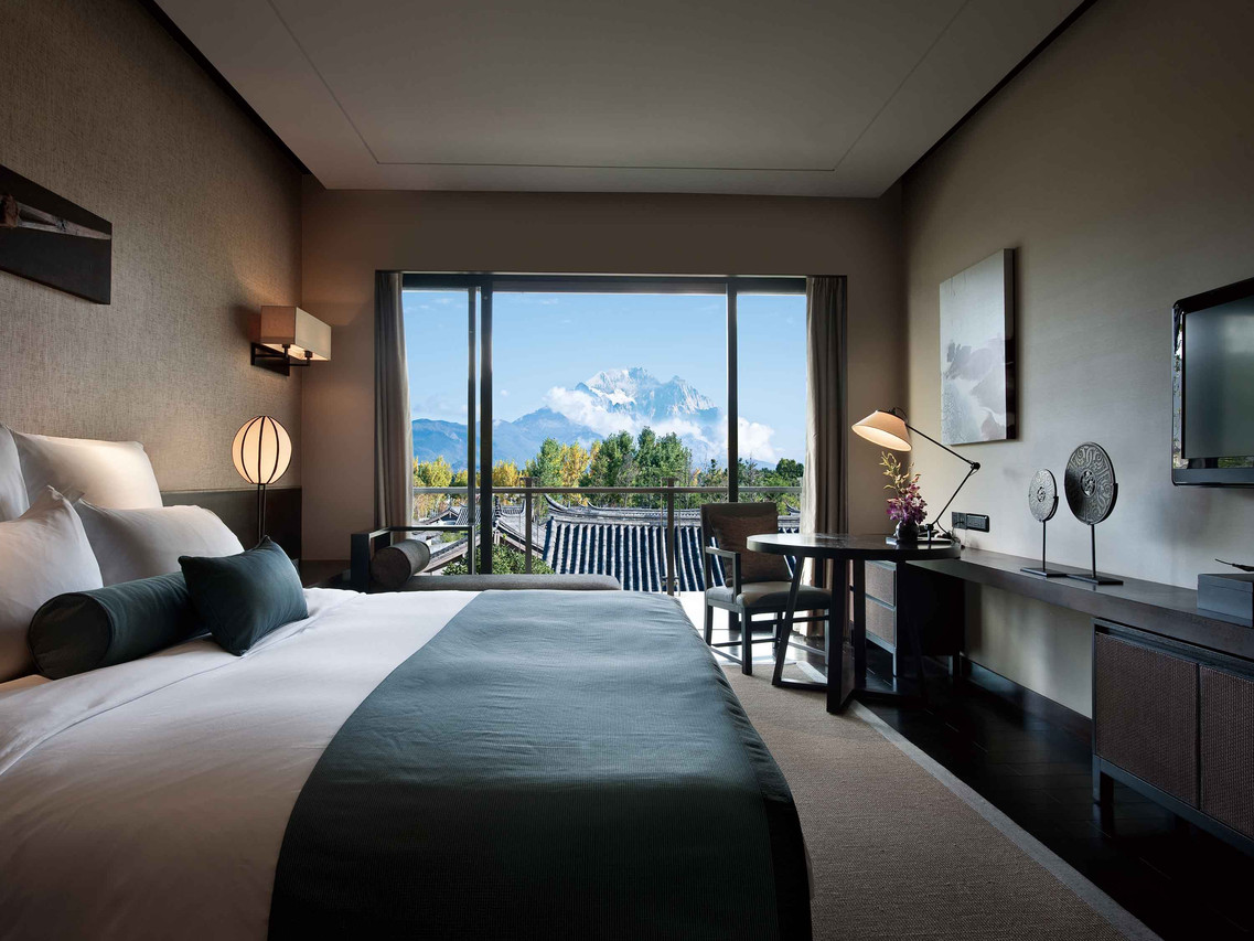 Pullman Lijiang Resort & Spa (丽江铂尔曼度假酒店) — an aerial view of the low-rise Naxi buildings, the garden lake, and Jade Dragon Snow Mountain behind