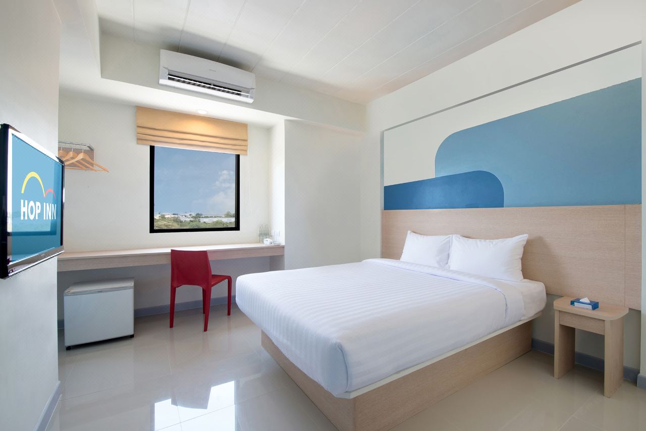 Standard Double room at Hop Inn Mahasarakham with a large bed, blue wave headboard wall, red chair, fridge and TV