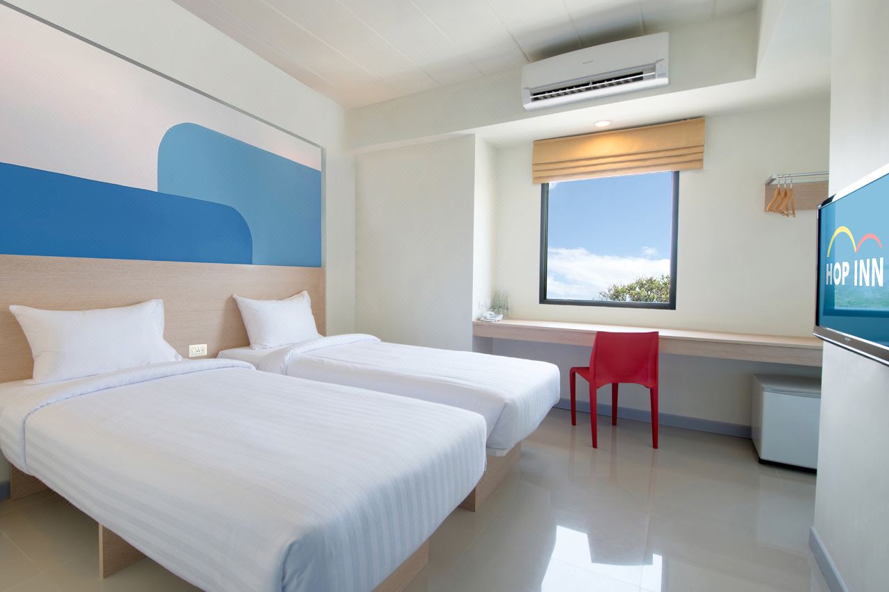 Standard Twin room with two single beds, a long desk, a red chair and a window looking outside