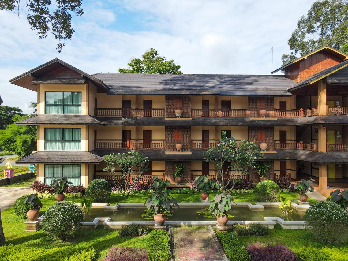อาคารห้องพักไม้สักสามชั้นของ Phumontra Resort กลางสวนพร้อมรางน้ำและกระถางดินเผา