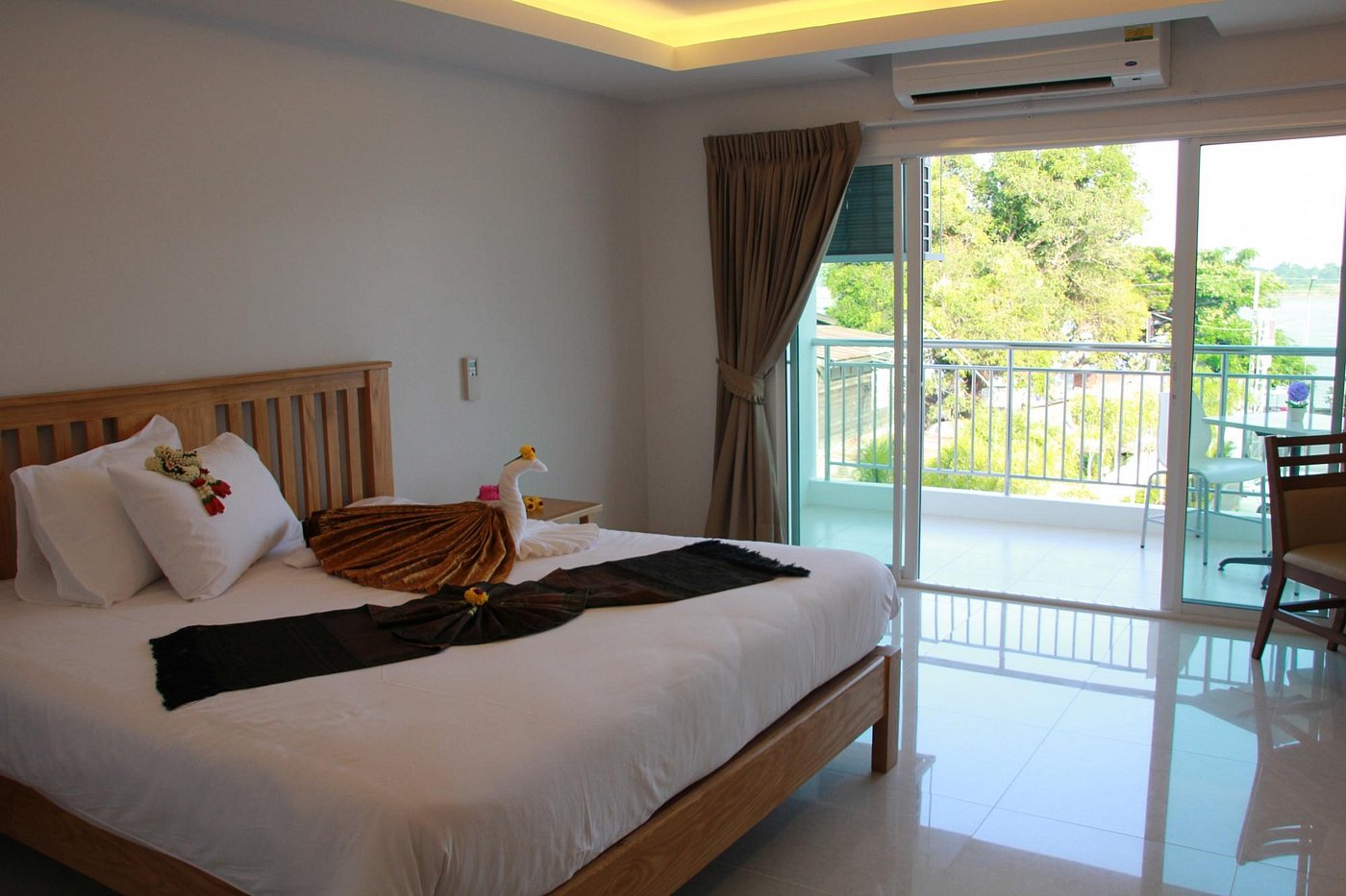 Deluxe room with natural-wood furniture, a large bed, and a balcony with sliding glass doors