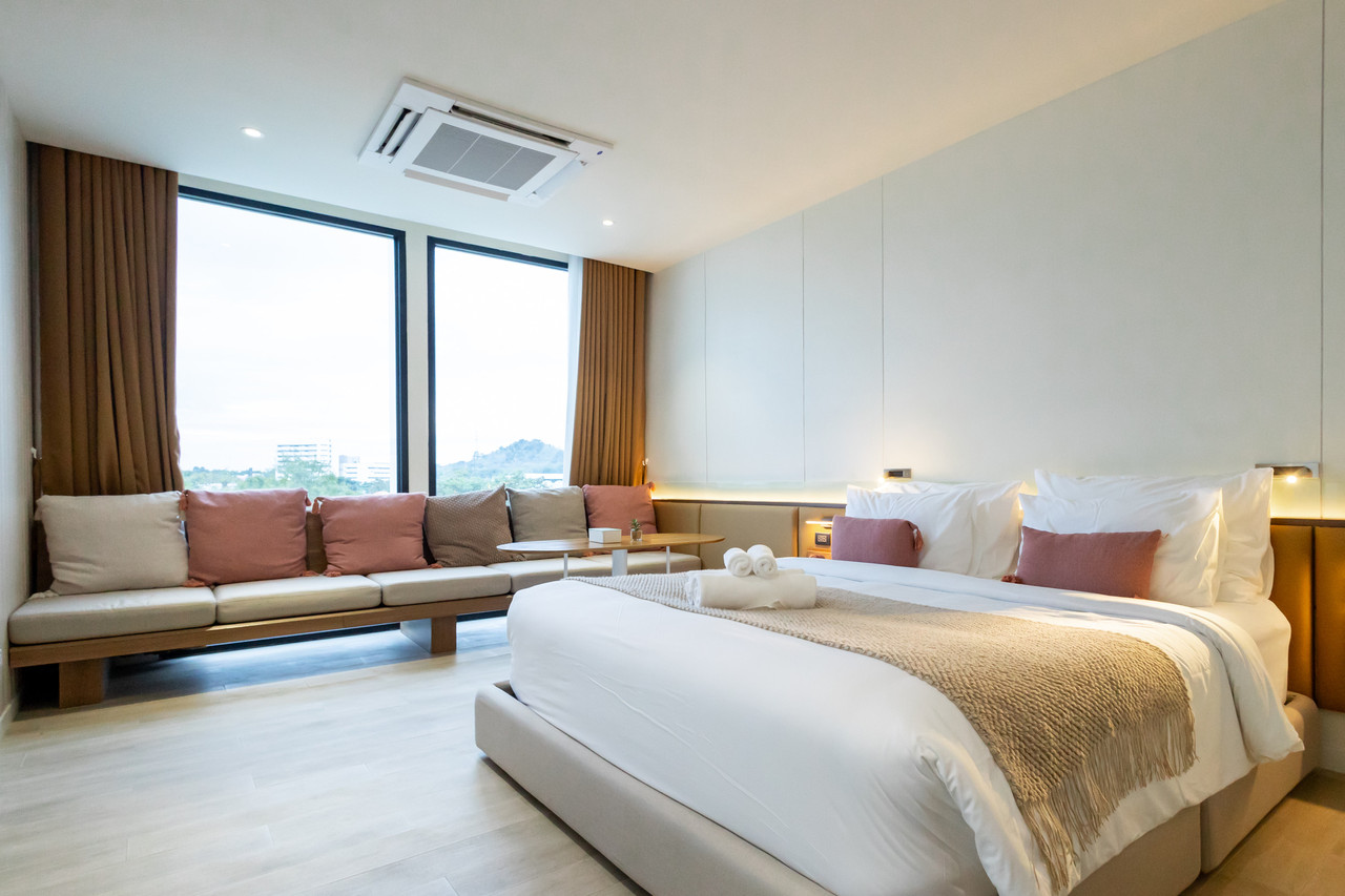 ห้อง Deluxe King เตียงนุ่มผ้าขาว มีโซฟายาวริมหน้าต่างกระจกบานใหญ่มองเห็นเขา