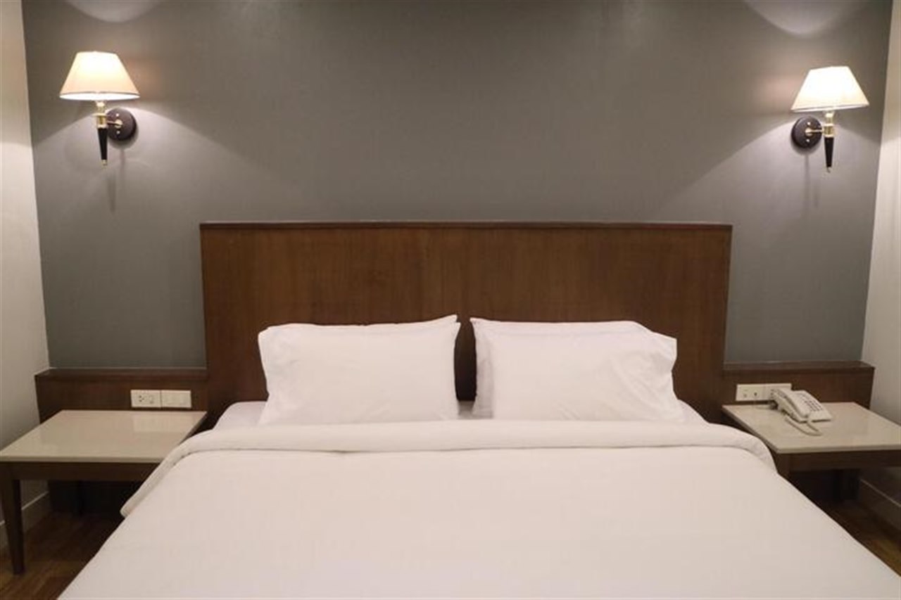 Grand Garden Hotel guest room with a large bed, wood headboard and twin bedside lamps