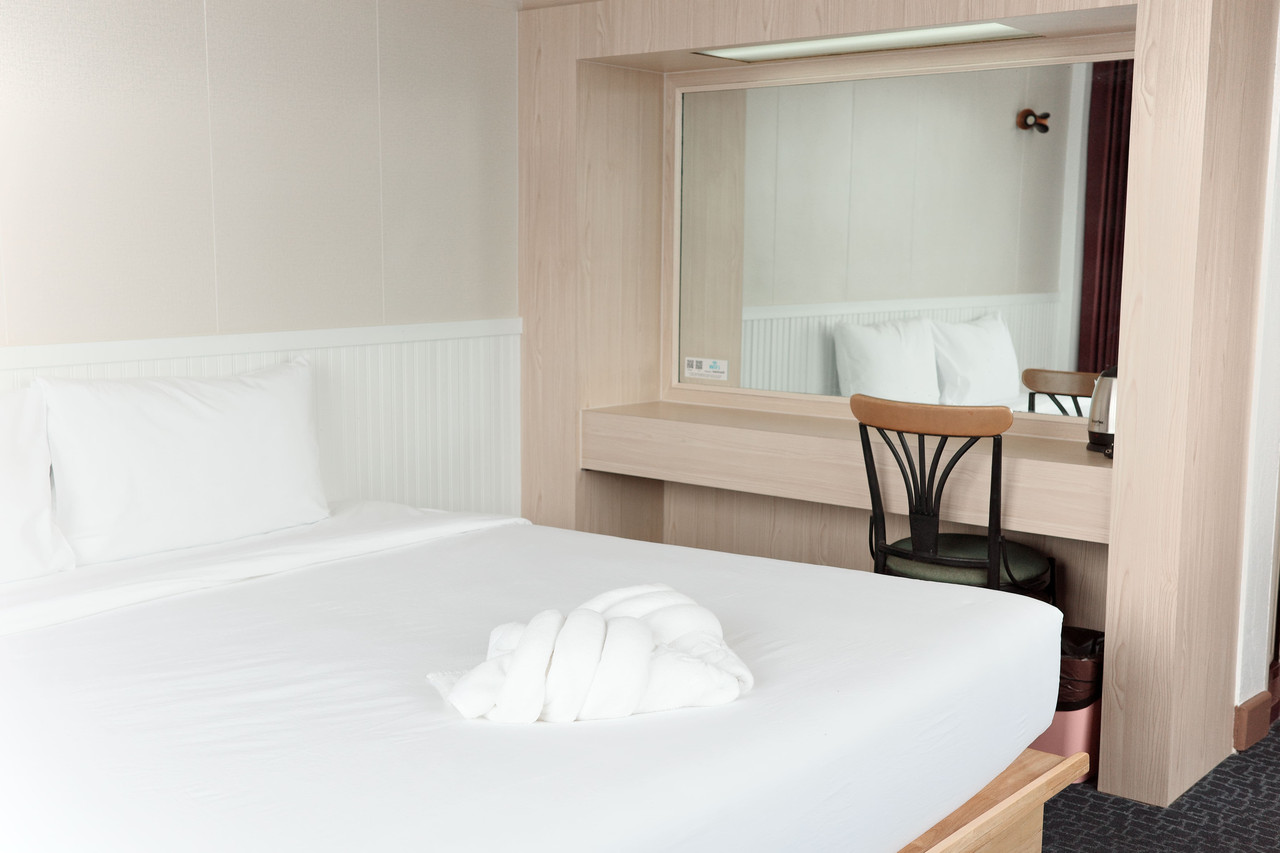 ห้องพักสะอาดของ Merlin Hotel เตียงปูผ้าขาว โต๊ะไม้และกระจก