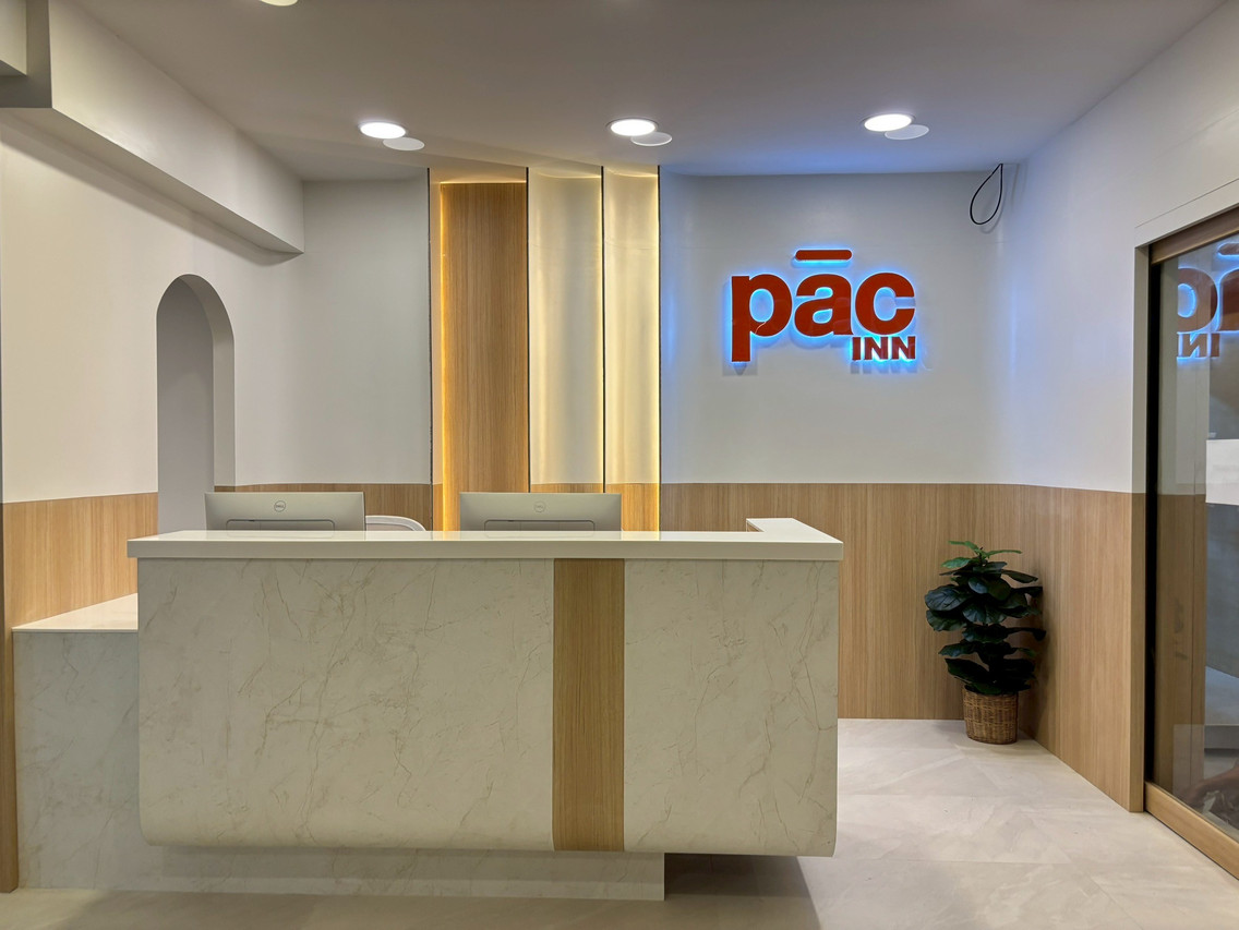 ล็อบบี้และเคาน์เตอร์ต้อนรับหินอ่อน ผนังบุไม้ ป้าย pāc INN เปิดไฟด้านหลัง