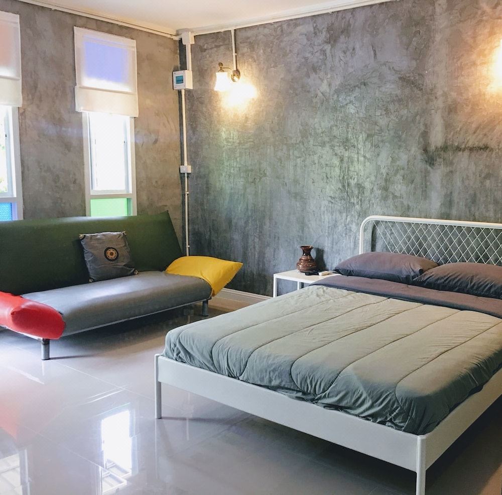 Nongbualamphu Signature guest room with bare polished-concrete walls, a large bed and sofa, and a glossy tiled floor